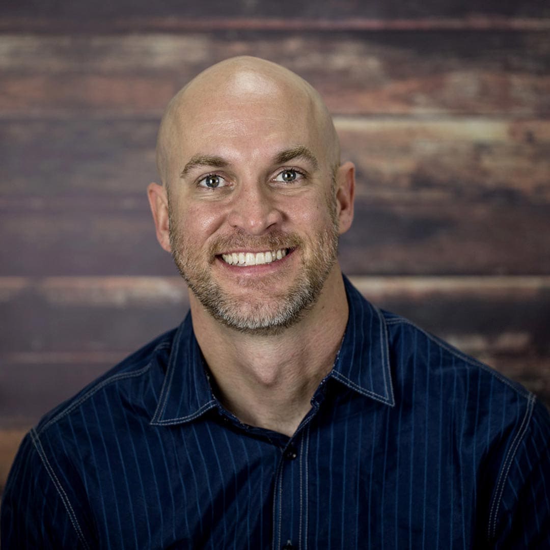 Portrait of Middle Aged Bald Man Wearing a Dark Shirt with a Wood Background representing David Womack working for Digital Media Collab